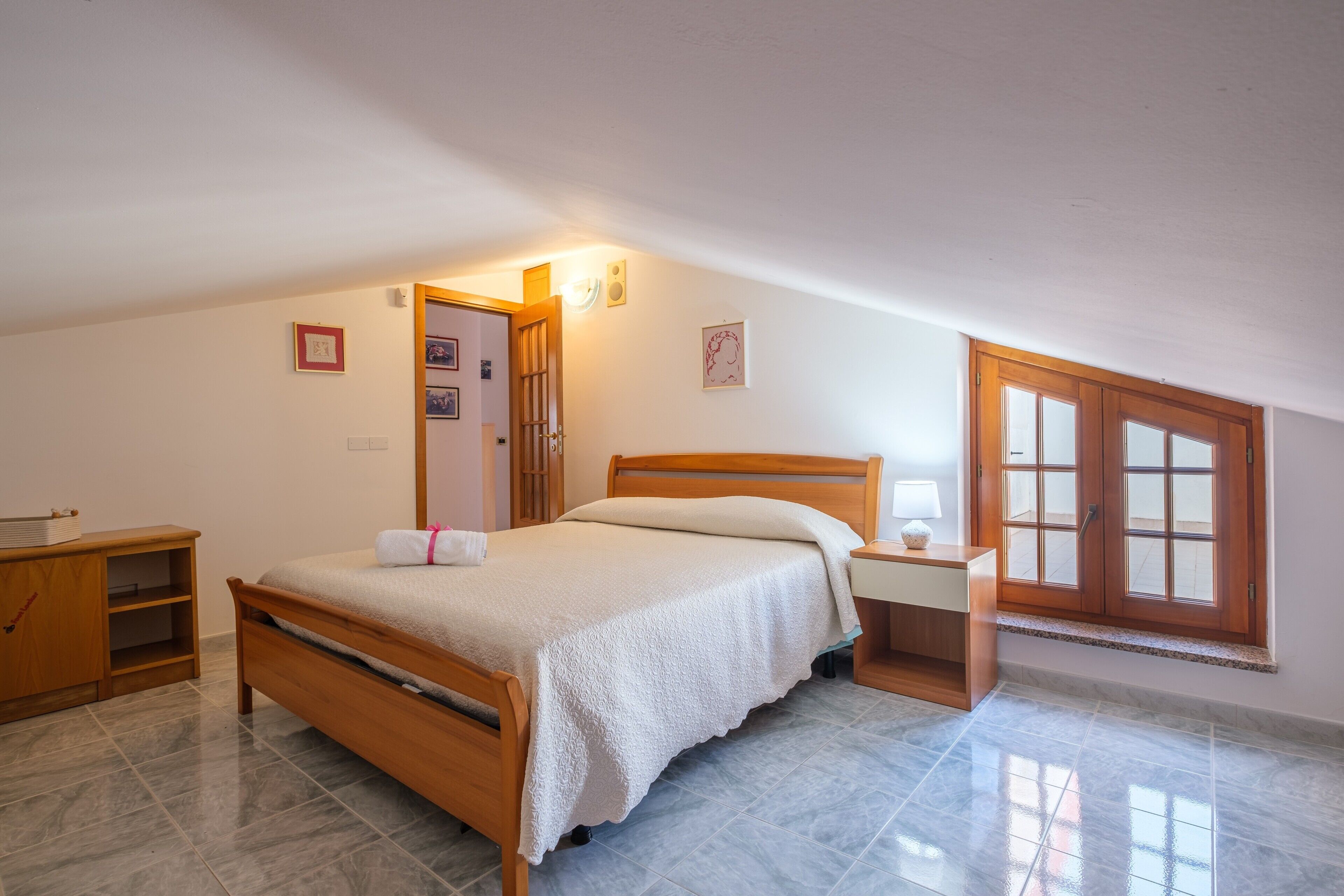 Un dormitorio con cama, mesita de noche, armario de madera y ventana con vistas.