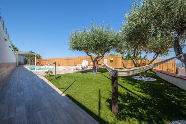 A backyard with a swimming pool, a hammock, and a wooden fence.