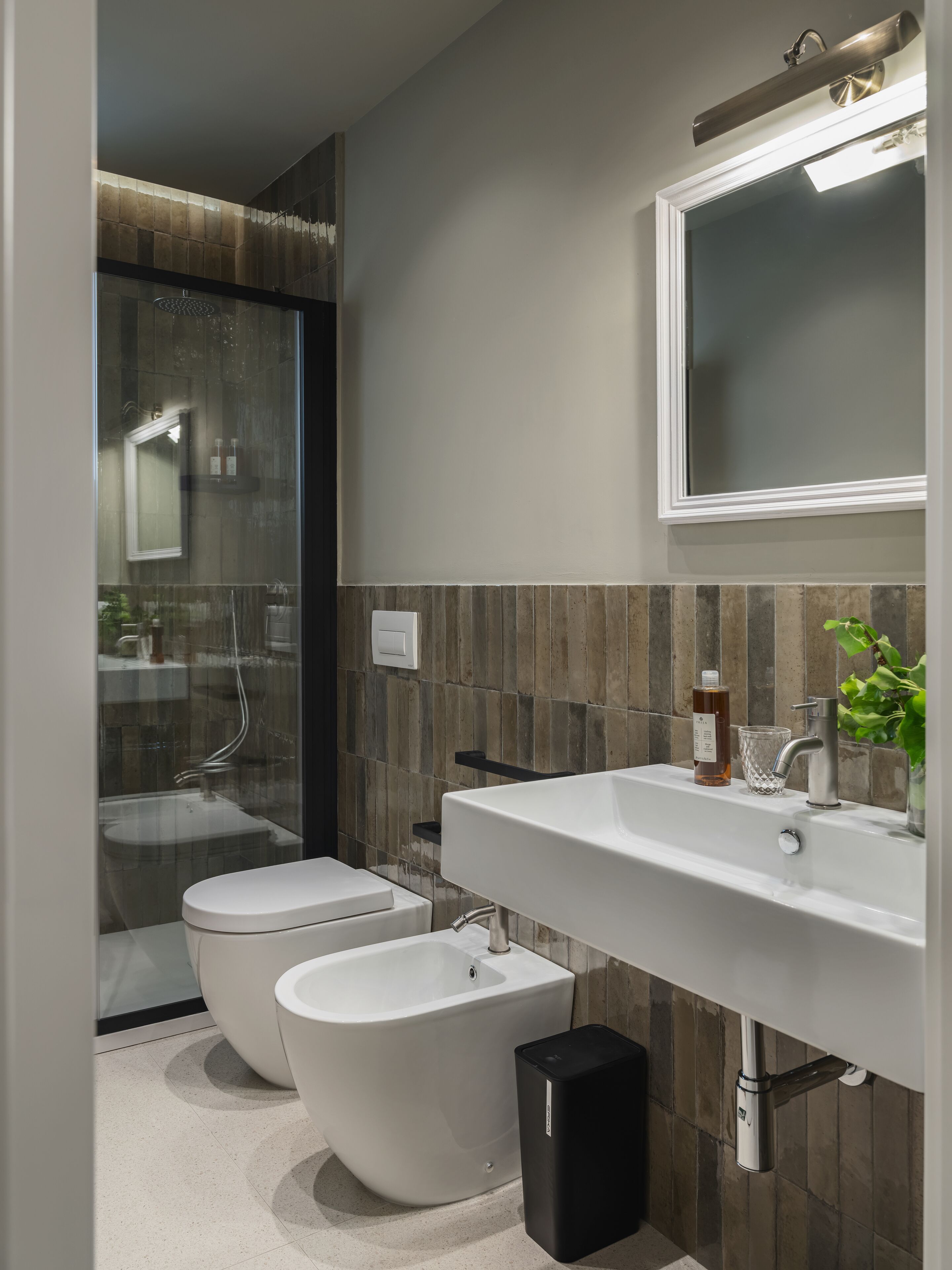 Een moderne badkamer met een douchecabine van glas, een wit toilet, een bidet, een grote spiegel en een wit wastafel met een kraan.