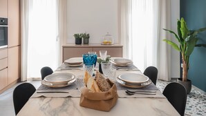 Een eetruimte met een marmeren tafel, borden, glazen en brood. Er staan potplanten en een raam met gordijnen.