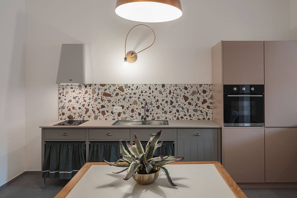 A modern kitchen with a terrazzo backsplash, a pendant light, a built-in oven, and a plant on the counter.