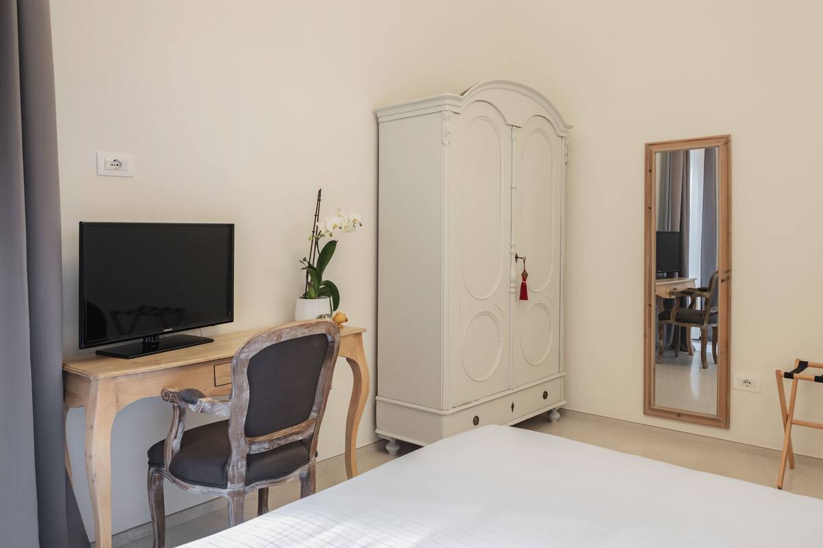 A hotel room with a bed, a desk with a television, a wardrobe, and a mirror.
