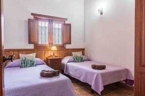 Une chambre avec deux lits, une tête de lit en bois, une table de chevet avec une lampe et une fenêtre avec des rideaux.
