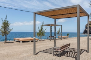 Un belvédère au bord de la plage, avec des bancs, une table en bois et une vue sur la mer.