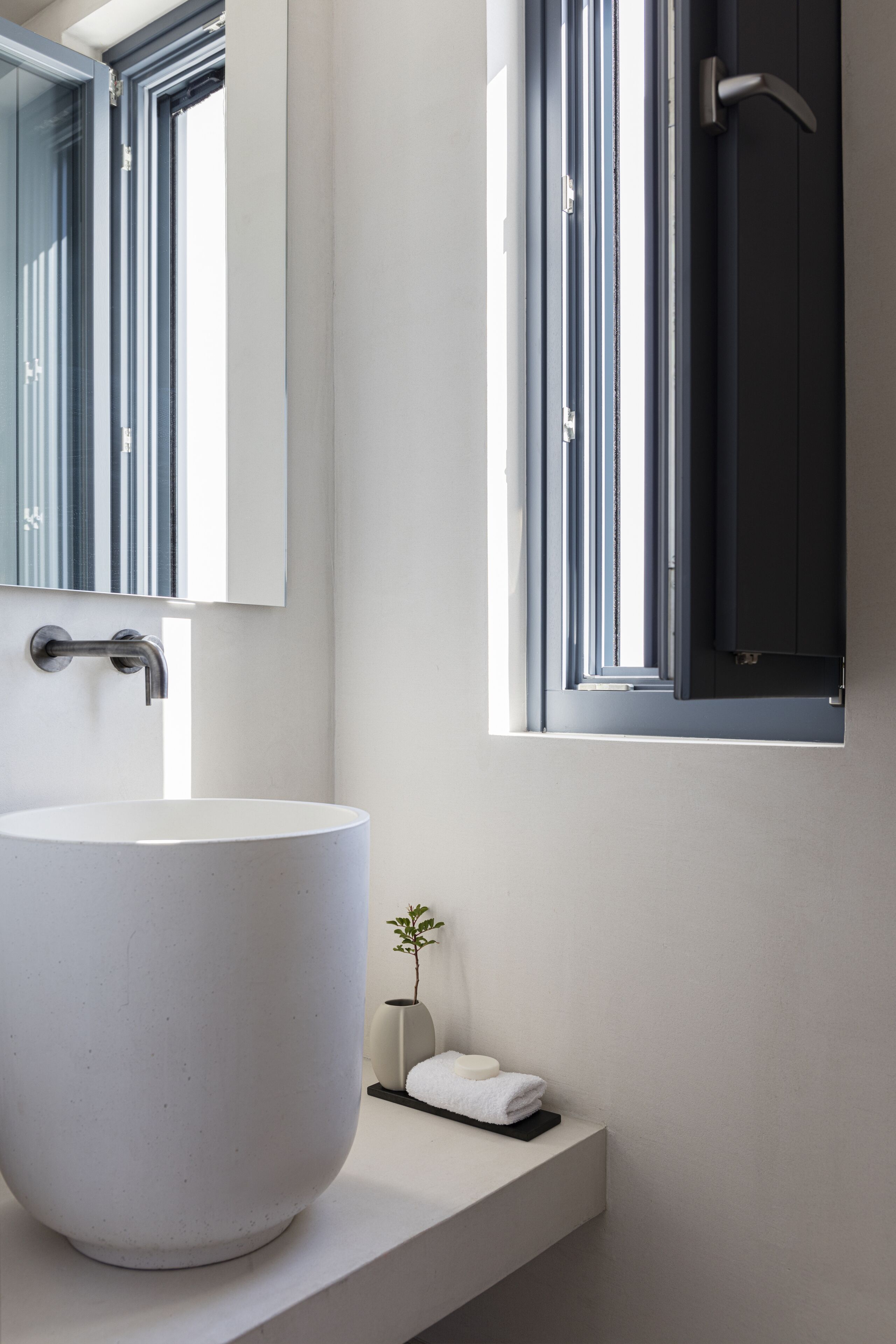 A modern bathroom with a large white sink, a mirror, and a window with a view of the outside.
