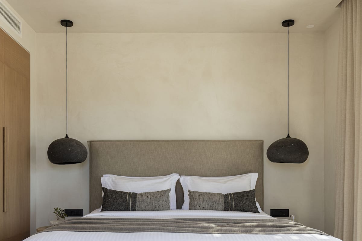 A modern bedroom with a large bed, two pendant lights, a wooden bench, and a ceiling fan.