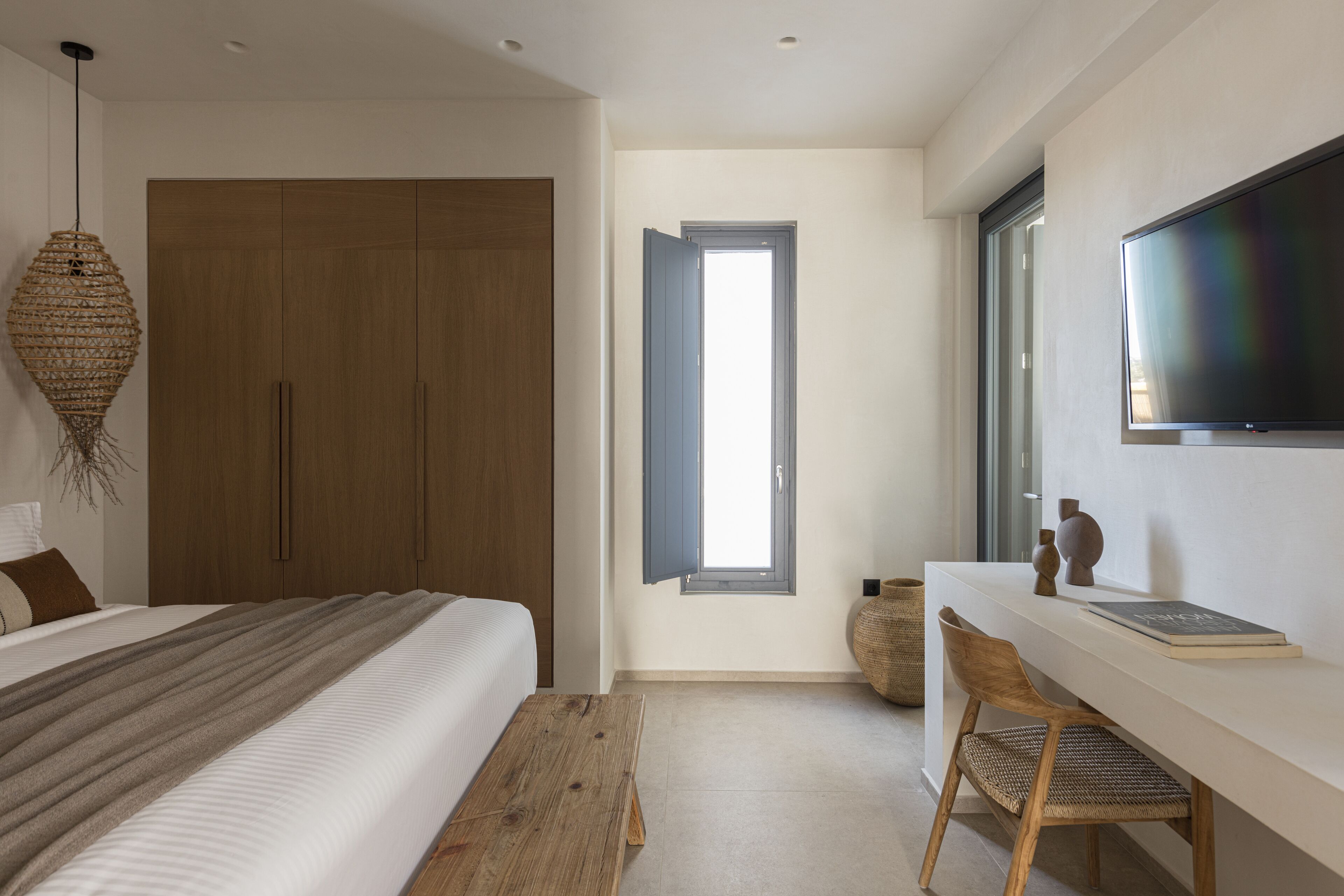 Un dormitorio con una cama grande, un armario de madera, un escritorio con silla y un televisor en la pared.