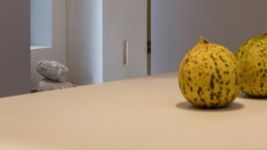 Ein modernes Interieur mit einer weißen Wand, einer hängenden Lampenschirm aus Gewebe und zwei gelb strukturierten Objekten auf einer Fläche.
