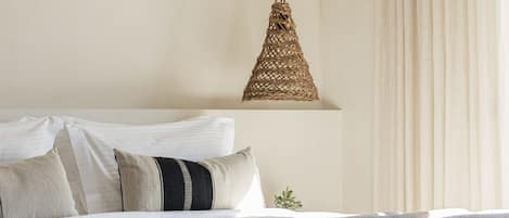 A neatly made bed with a wooden headboard, a woven pendant light, and a view of a window with curtains.
