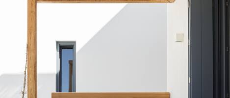 A wooden table and bench set under a bamboo roof, with a white wall and a door in the background.