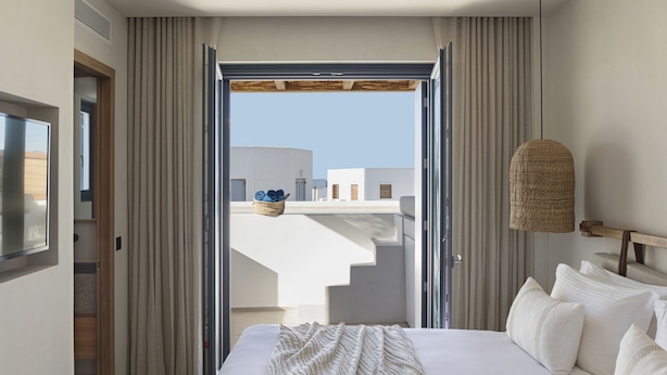 Ein Hotelzimmer mit Bett, Blick ins Freie und einem Balkon mit Korbstuhl.