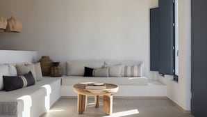 Ein modernes Wohnzimmer mit einem weißen Sofa, einem Holztisch und einem großen Fenster mit dunklen Rollläden.