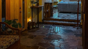 Un interior acogedor con suelo de piedra, techo de madera y una zona de cocina con refrigerador y televisor.