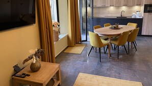 Una cuina moderna amb armaris de fusta, una zona de menjador amb cadires grogues i un televisor penjat a la paret.