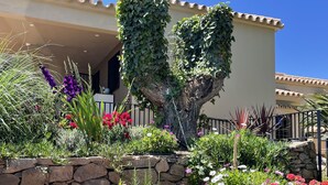 Un jardí amb una varietat de flors i plantes, una paret de pedra i un edifici amb teulada d'estil clàssic.