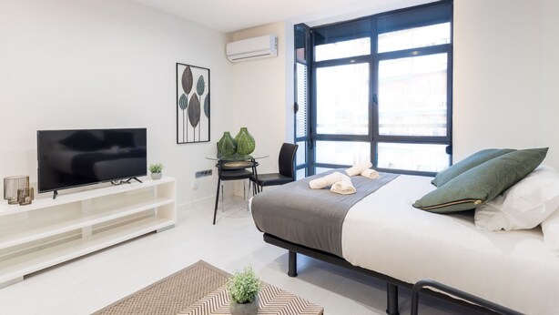 A modern bedroom with a bed, TV, and a large window. - La Latina studio in the heart of Madrid (Madrid)