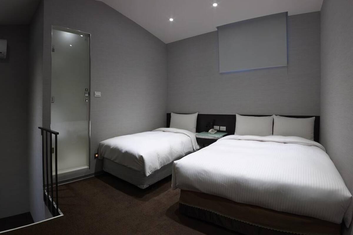 A hotel room with two beds, a small bedside table, a wall-mounted TV, and a door with a glass panel.