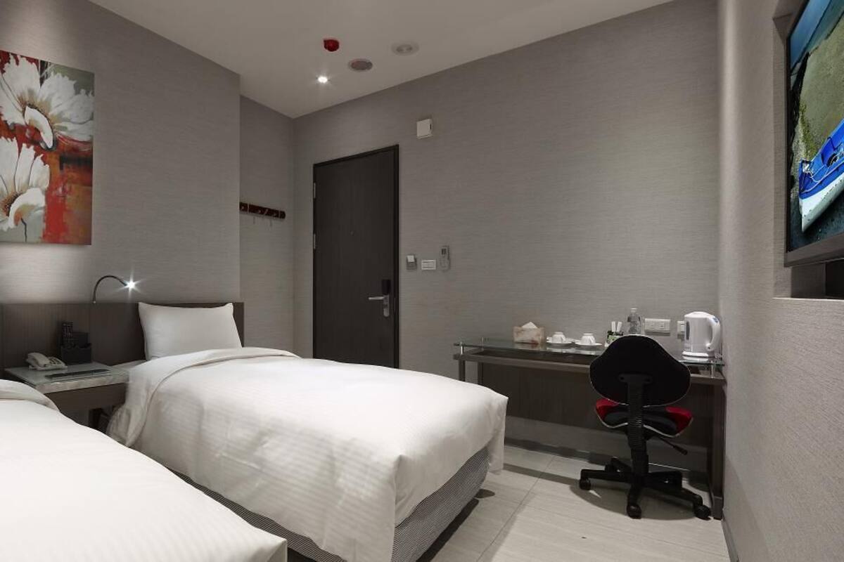 A hotel room with two beds, a desk with a chair, a television, and a door.