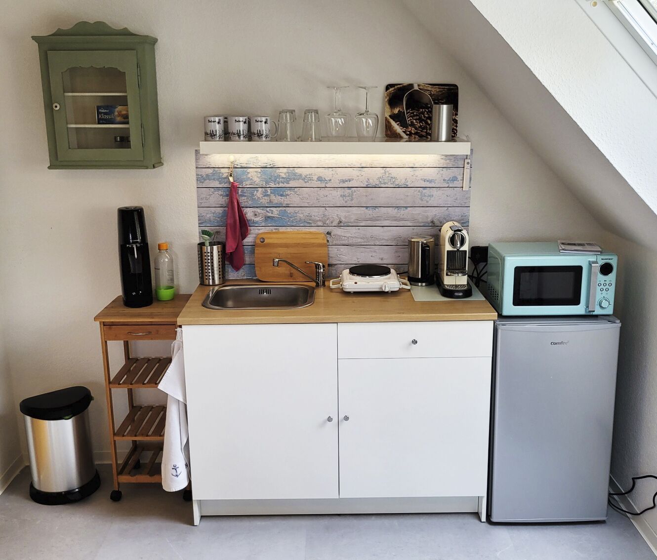 A compact kitchen with a wooden countertop, a sink, a small fridge, a microwave, and a cabinet above the counter.