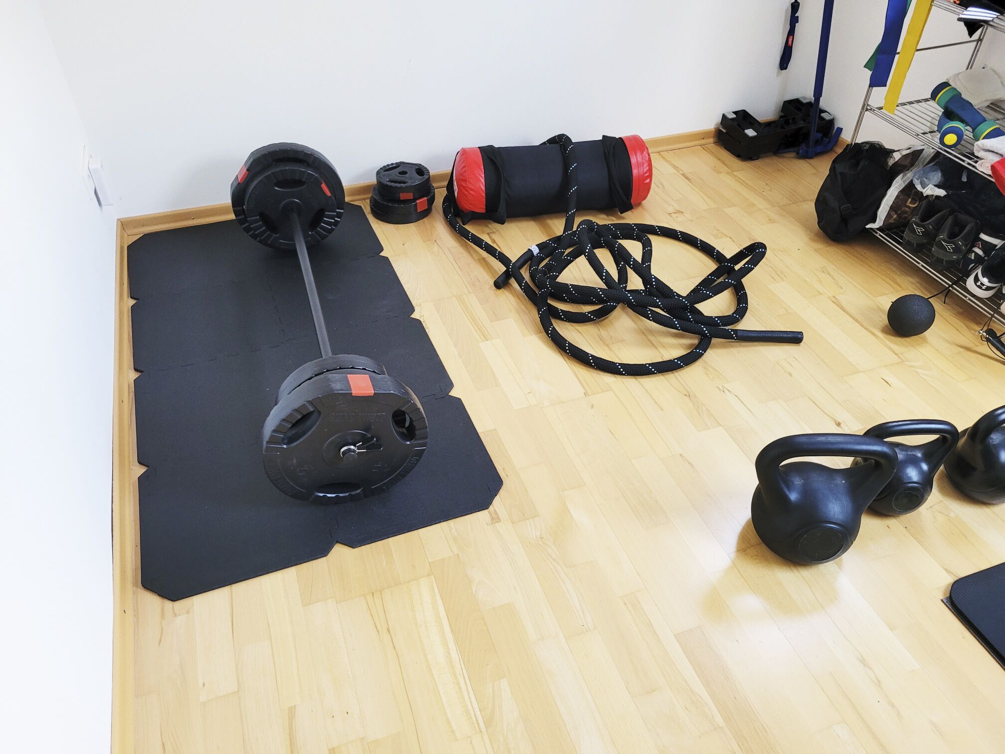 Un gimnasio con barra, mancuernas, colchoneta para yoga y un soporte para pesas.
