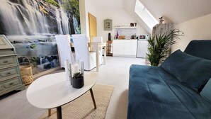 A modern living room with a blue sofa, a white coffee table, and a painting of a waterfall. There is a kitchen area with cabinets and a microwave. - Vacation apartment between the North Sea and the Baltic Sea - Fitness room (Ostenfeld)