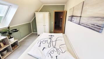 Ein Schlafzimmer mit einem Bett, einer Zimmerpflanze, einem Kleiderschrank und einem Bild an der Wand.
