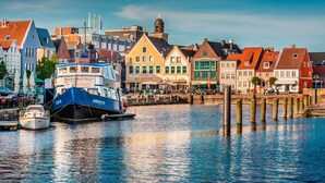 A waterfront with a blue and white boat docked at a pier, surrounded by colorful buildings with distinct architectural styles. - Vacation apartment between the North Sea and the Baltic Sea - Fitness room (Ostenfeld)