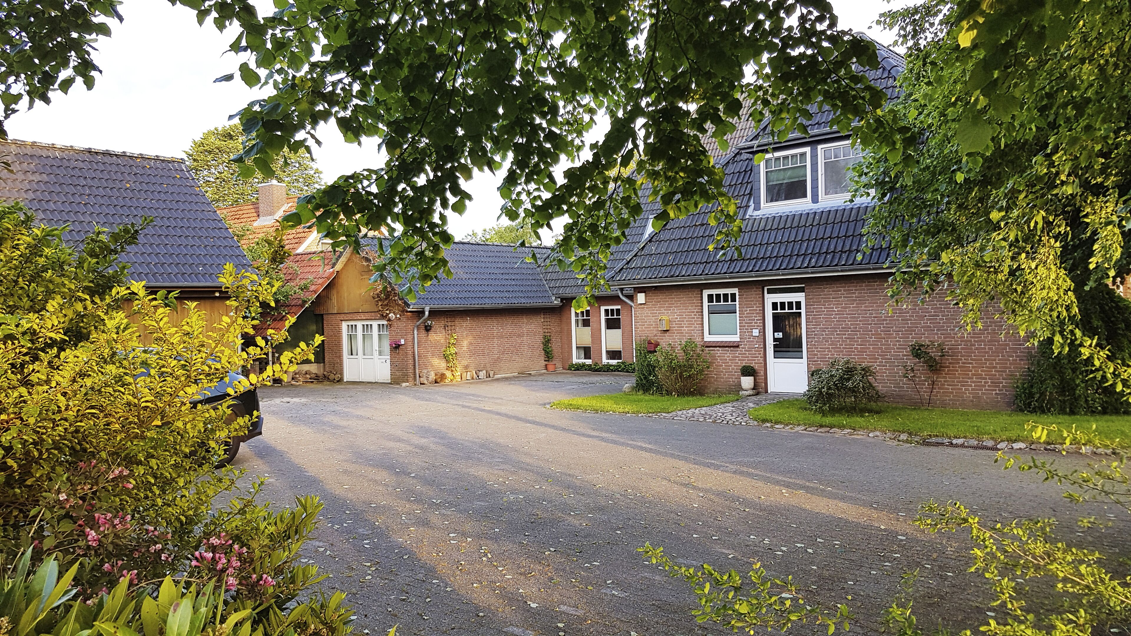 A residential property with a paved driveway, brick houses, and surrounding greenery.