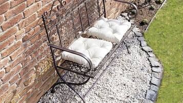 A metal bench with cushioned seats against a brick wall, surrounded by a gravel path and a grassy border.