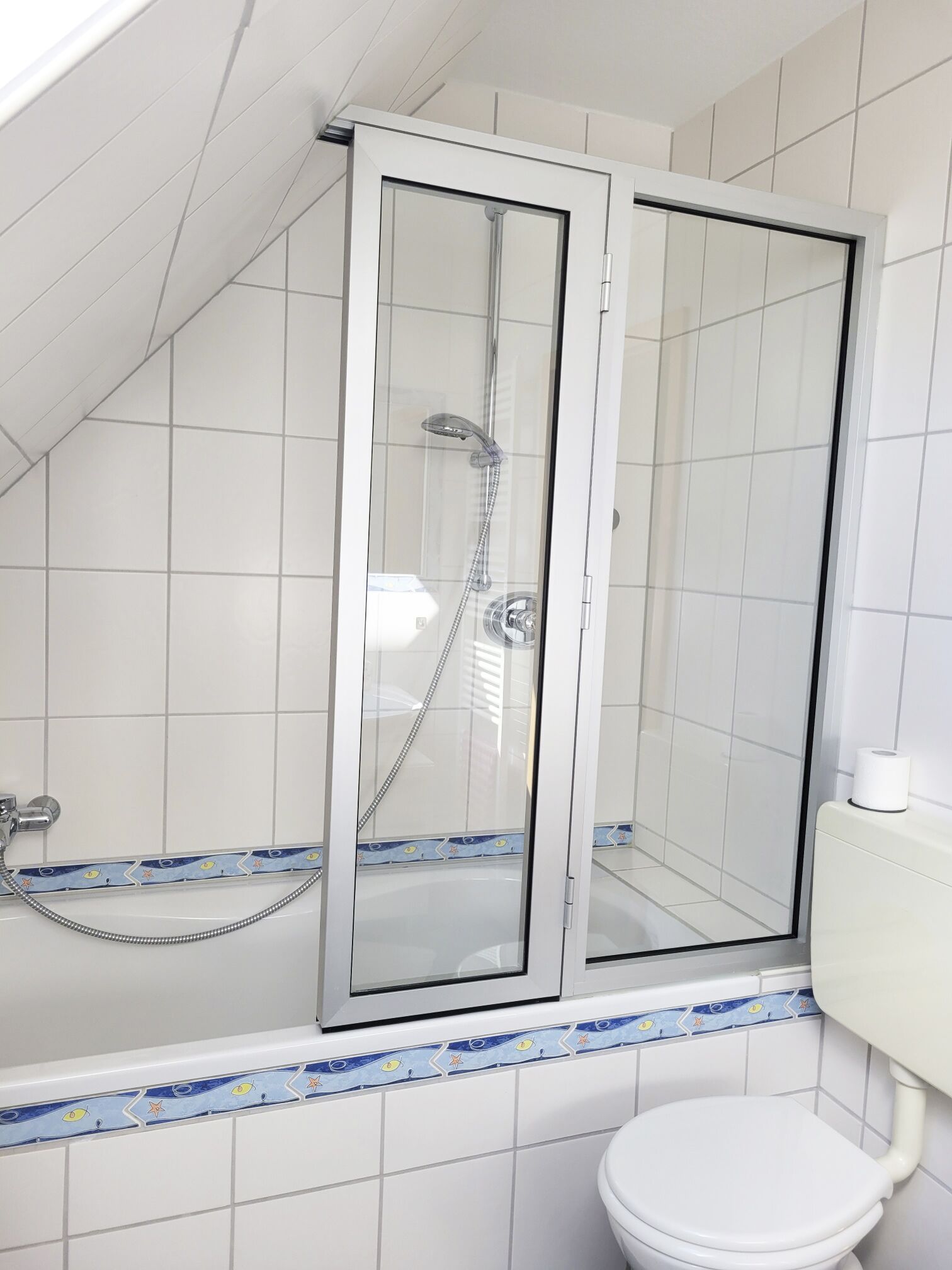 Aseo con cabina de ducha con puerta de vidrio, inodoro y bañera con un detalle de azulejos decorativos.