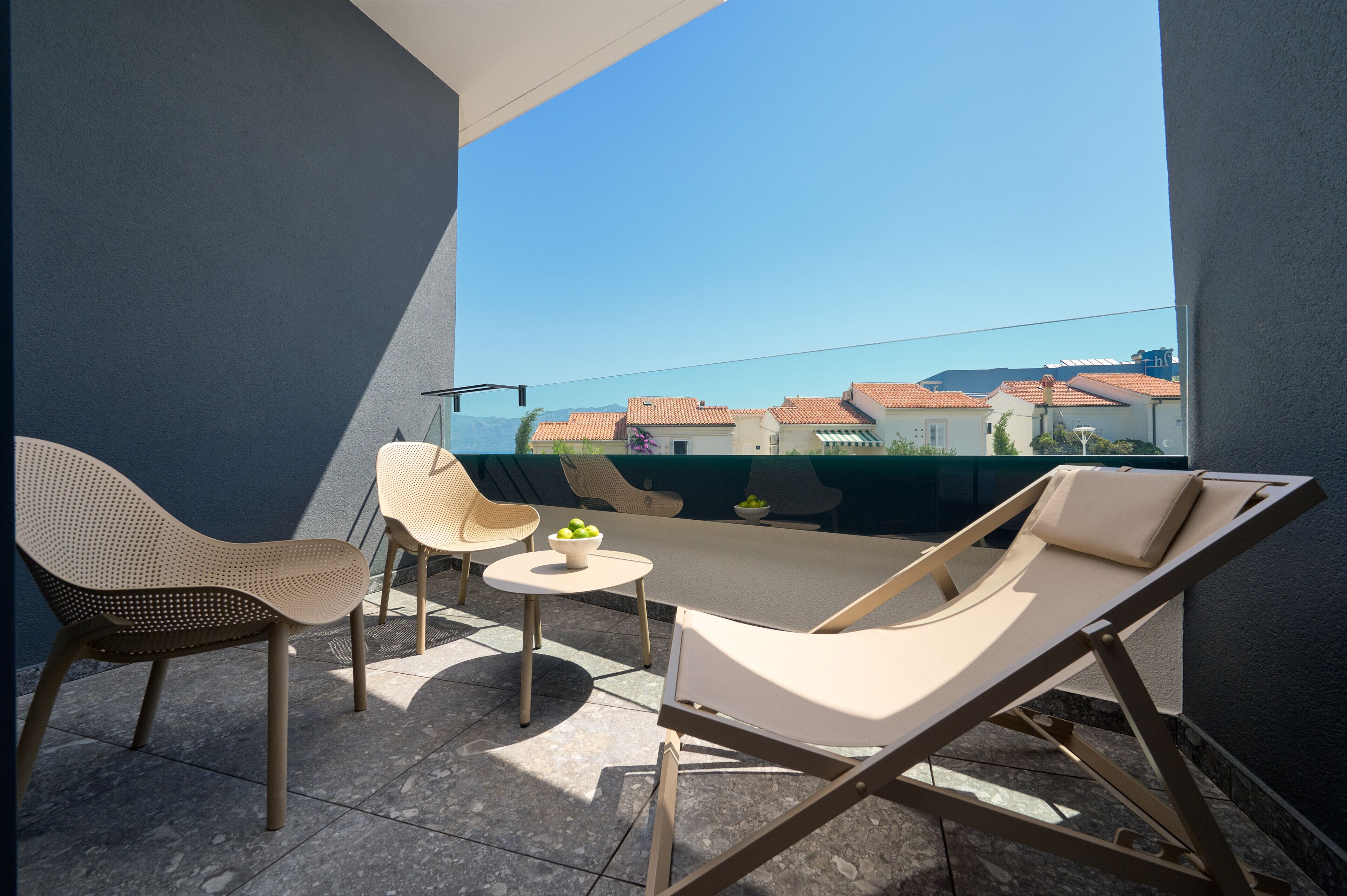 Ein Balkon mit zwei Loungestühlen, einem kleinen runden Tisch und einer Obstschale.