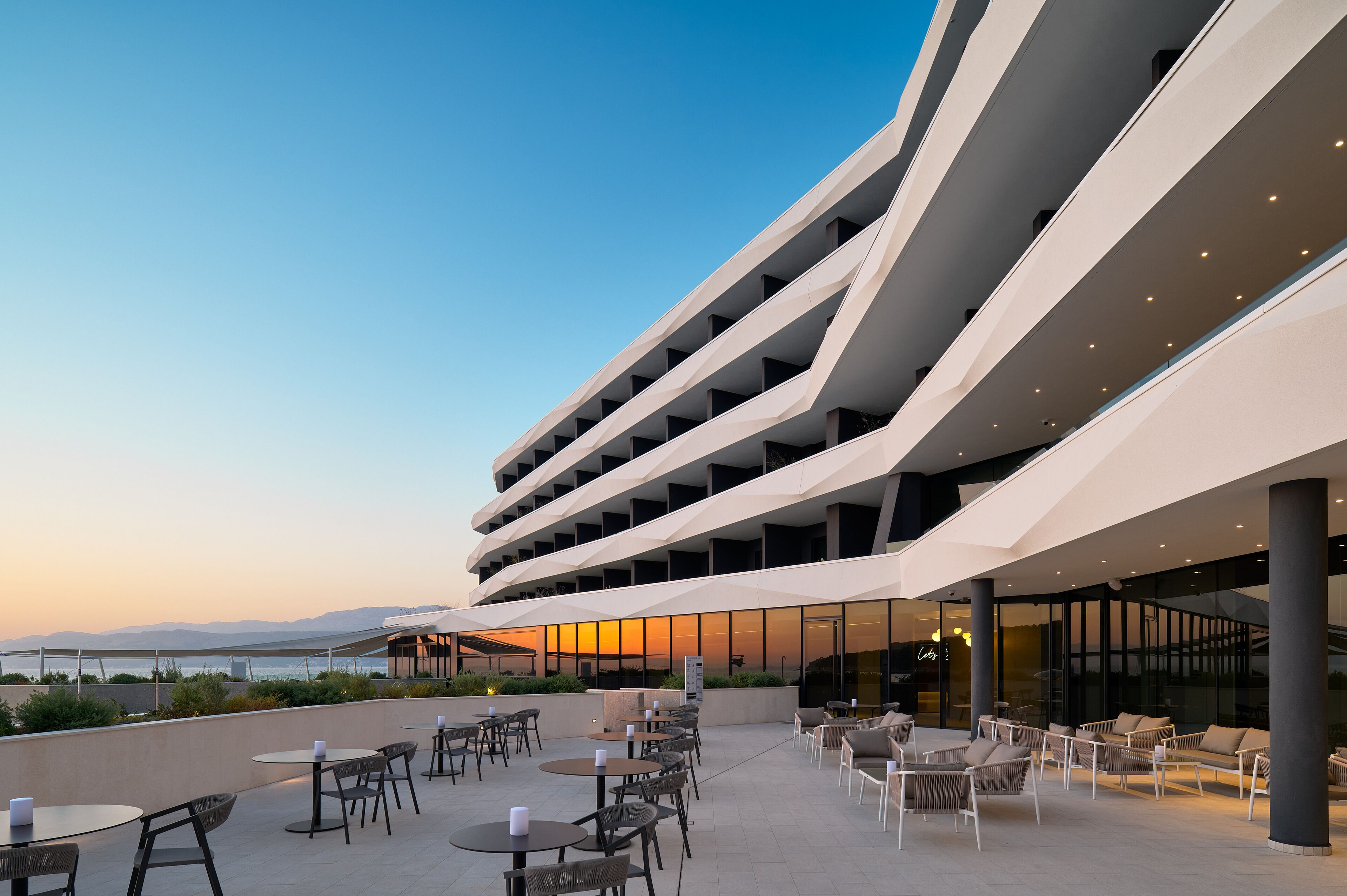 A modern building with multiple balconies, outdoor seating, and a view of the sea.