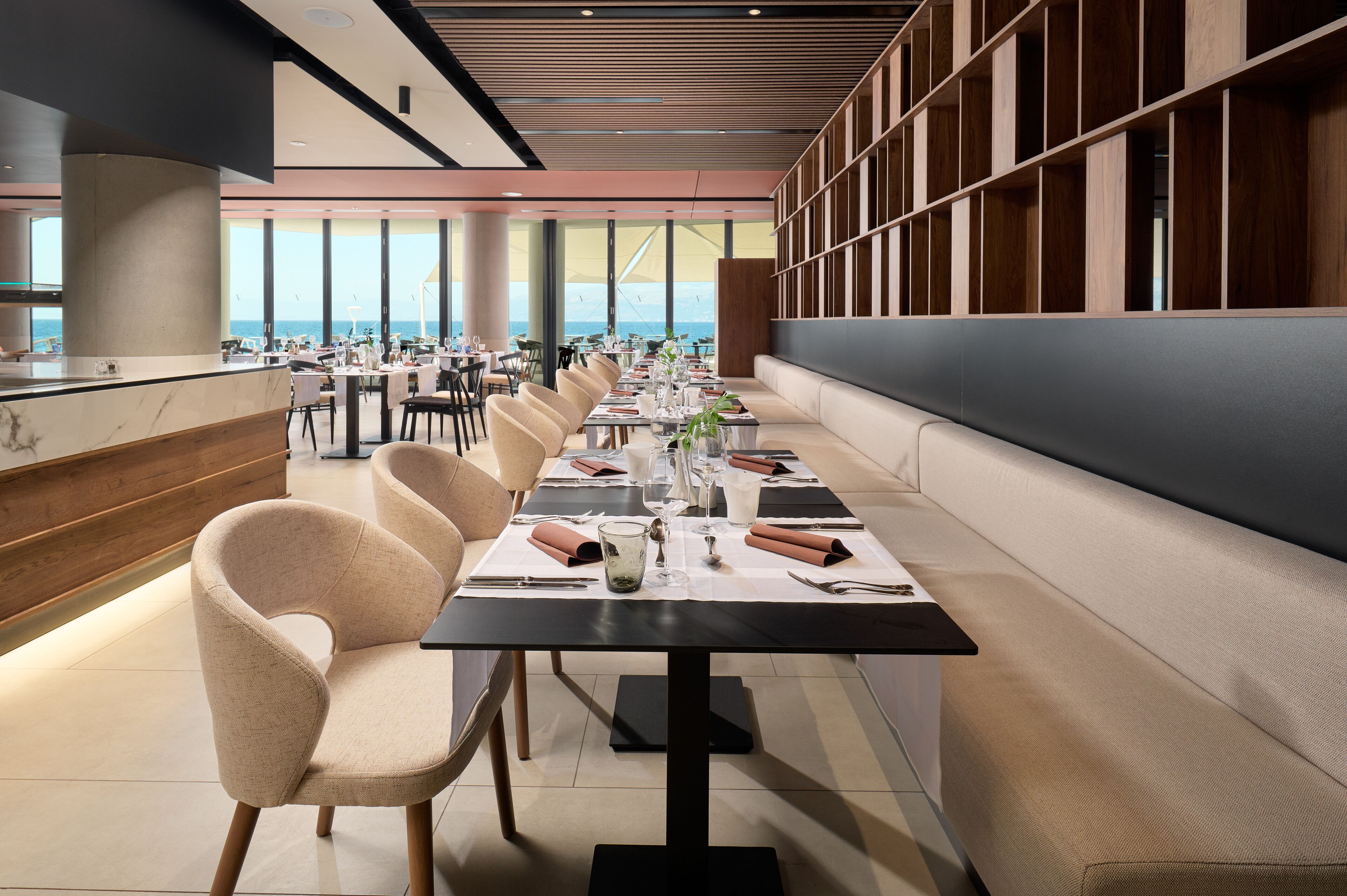 A modern dining area with a long table set for a meal, overlooking a scenic view.