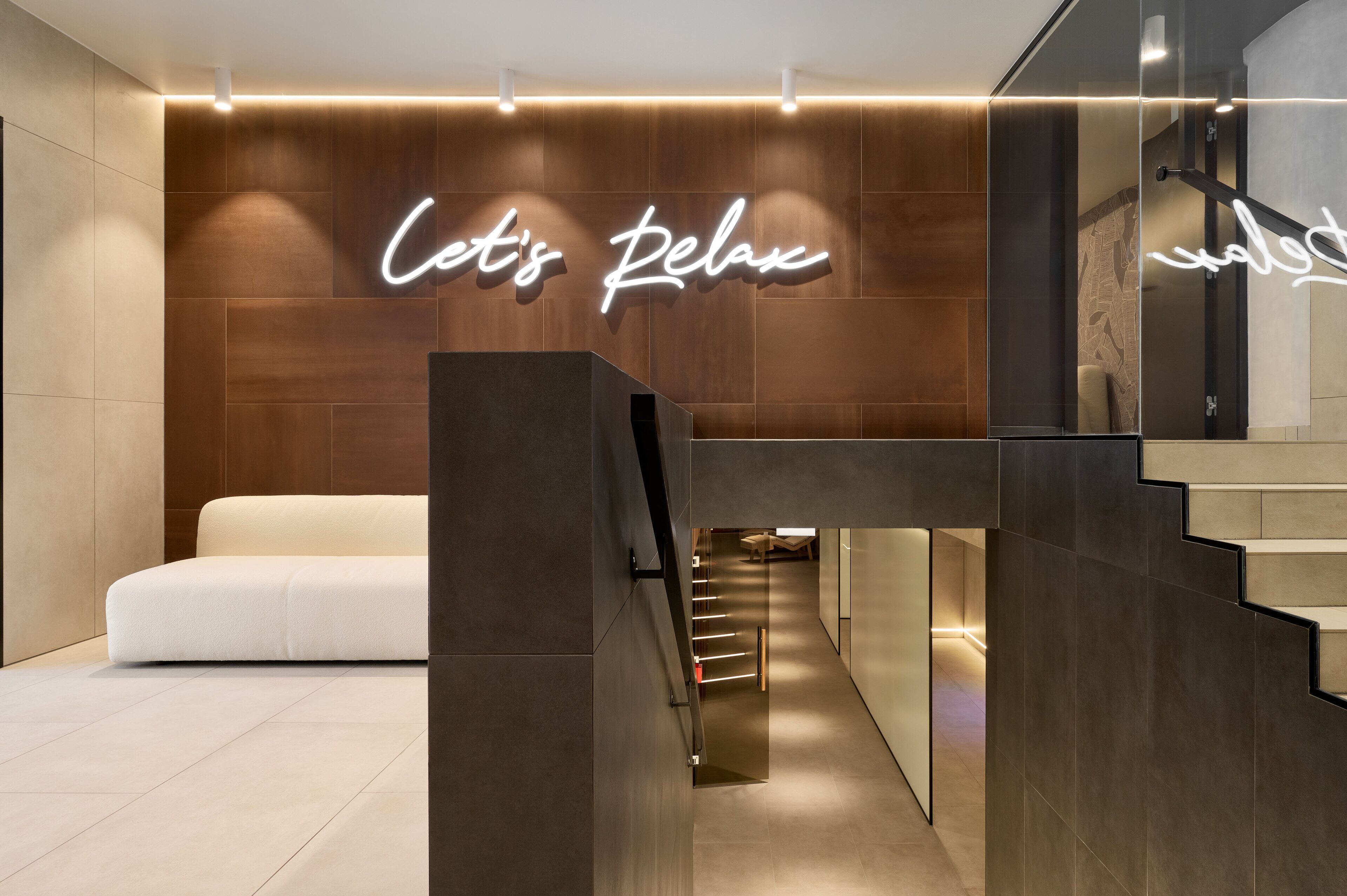 Un moderno vestíbulo de hotel con un letrero que dice 'Let's Relax', una escalera y una zona de estar.