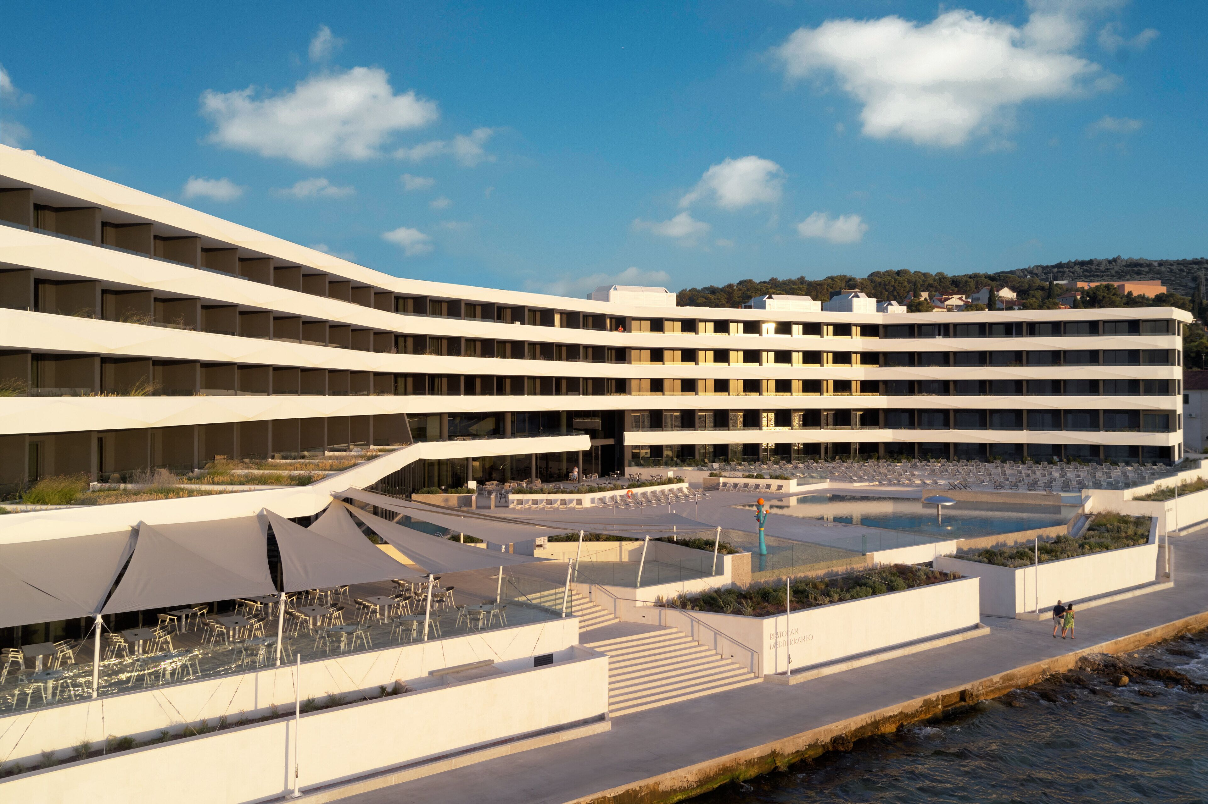 Een modern hotel met meerdere verdiepingen, buiten zitplaatsen en een zwembad.