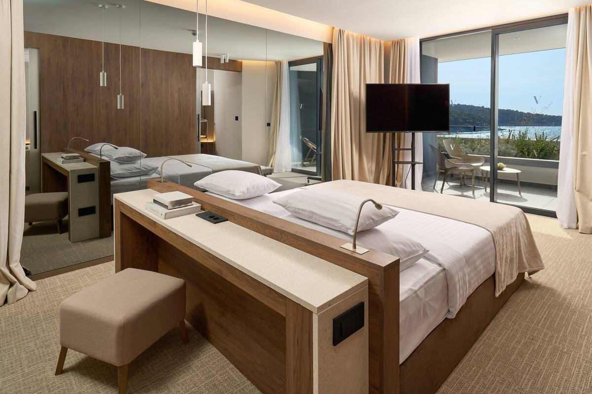 A modern hotel room with a large bed, a desk, and a balcony with a view.