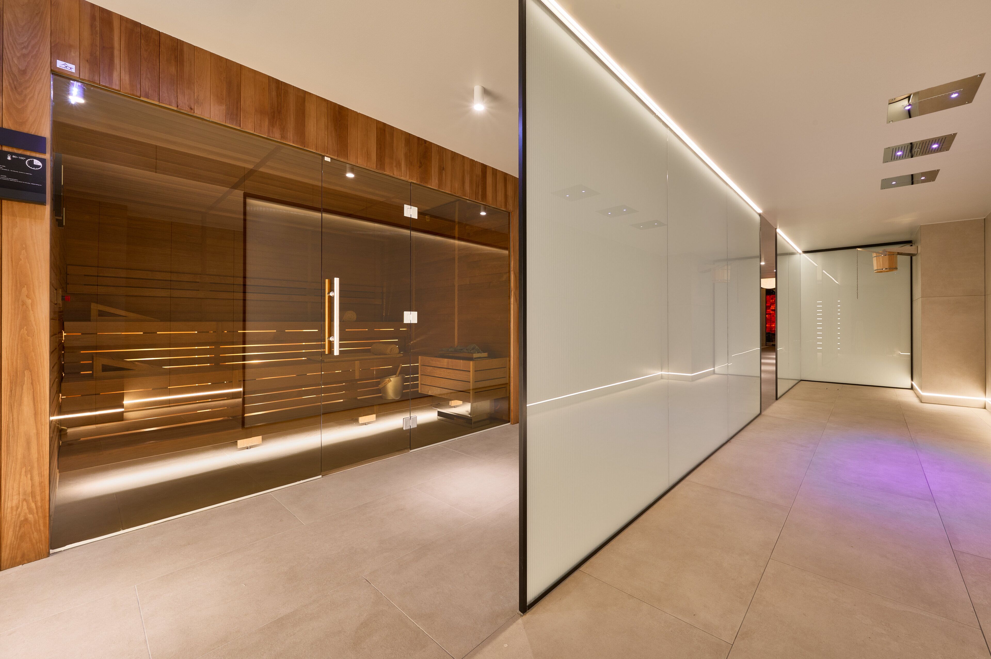 Un couloir d’hôtel moderne avec un mur lambrissé en bois, une cloison en verre et un plafond élégant et éclairé.