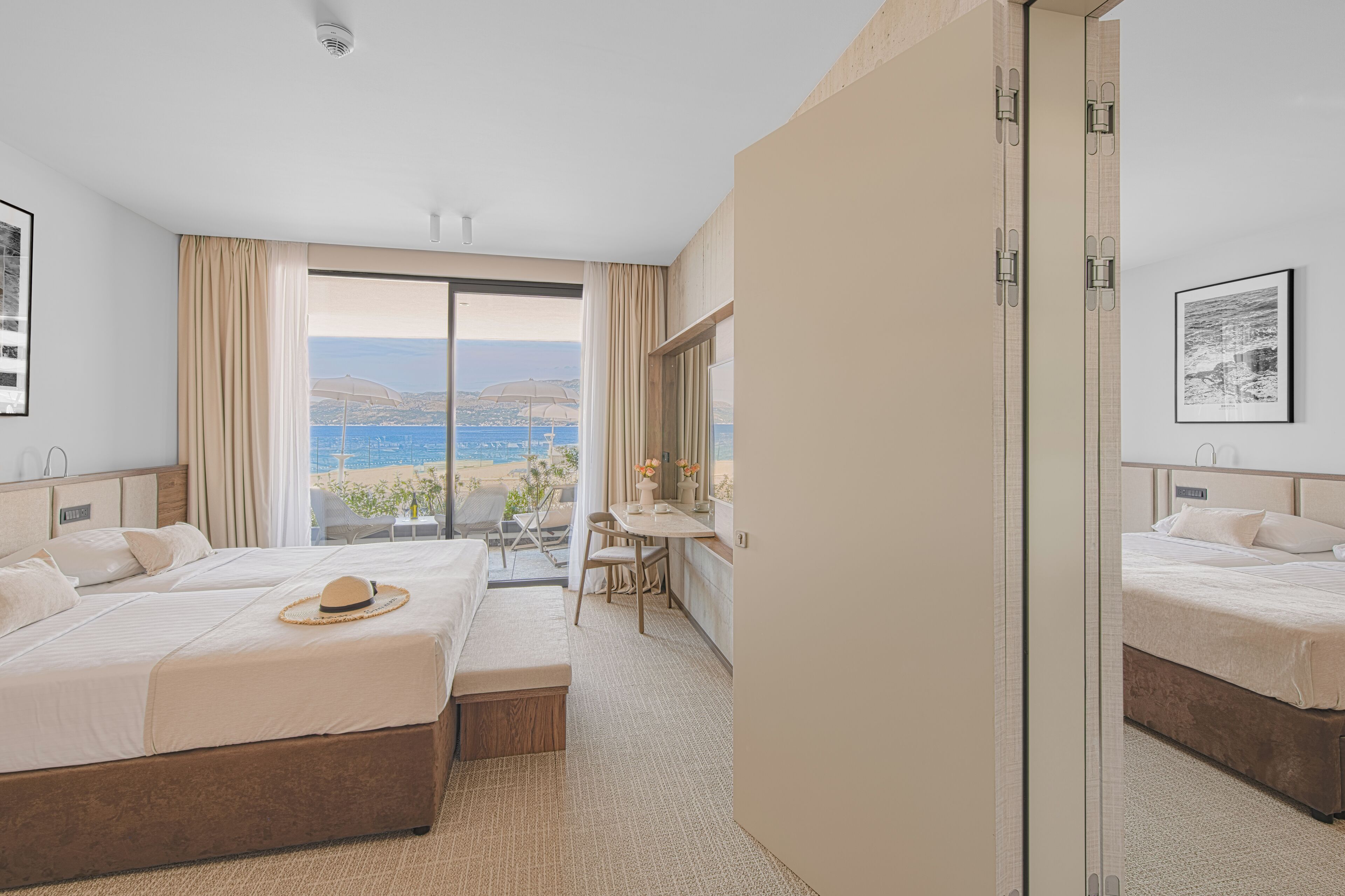 Een hotelkamer met twee bedden, een bureau en uitzicht op het strand.