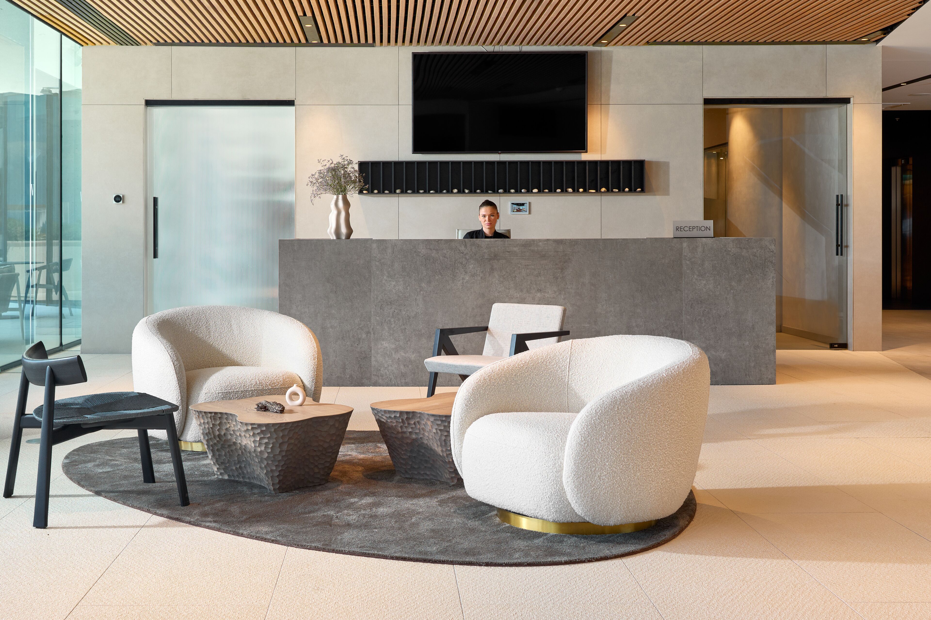 Un espace d’accueil moderne comprenant un comptoir de réception, un grand téléviseur à écran plat et des sièges, notamment un fauteuil blanc et une chaise noire.