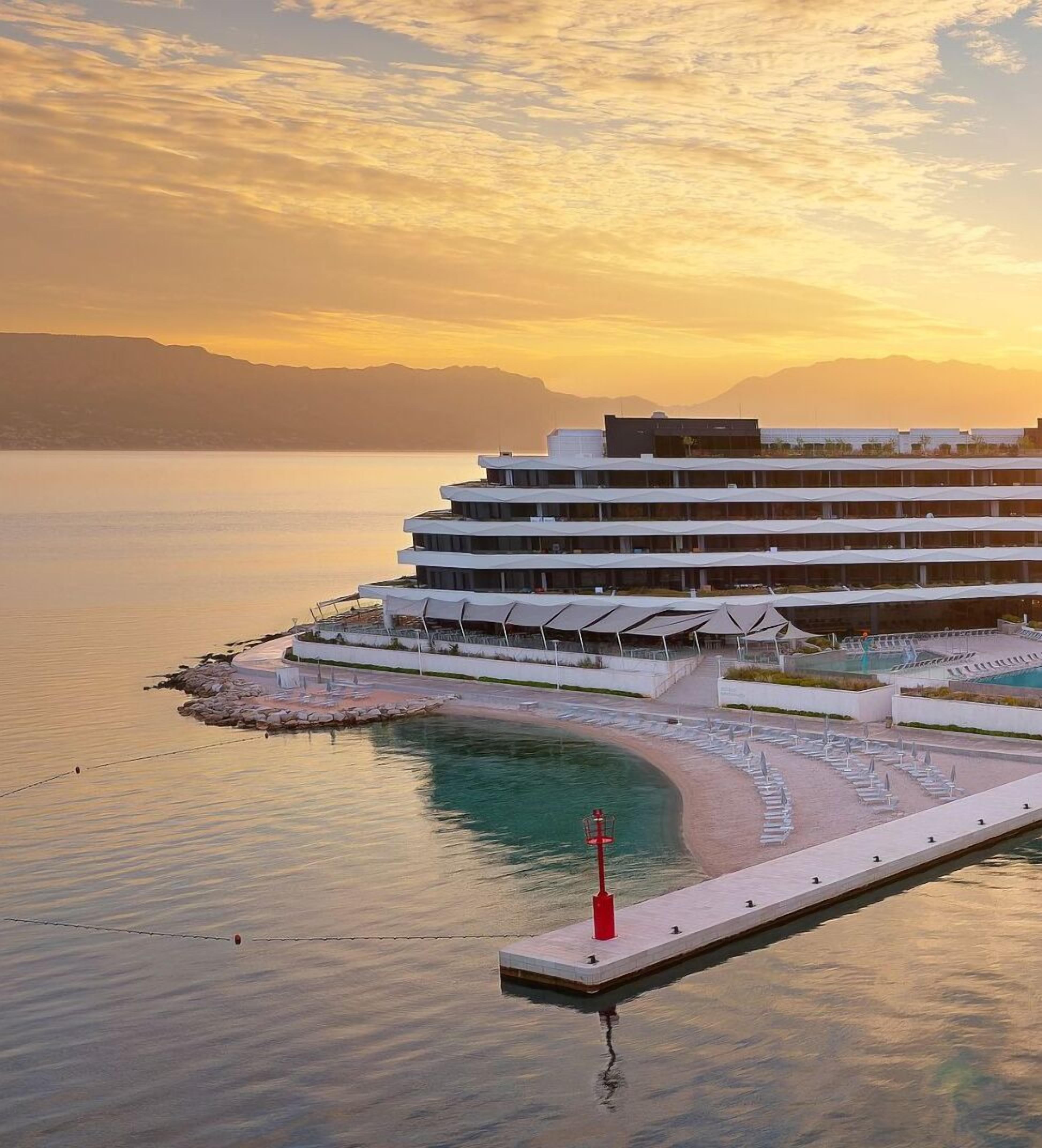 A modern cruise ship with multiple decks and a waterfront promenade with sun loungers.