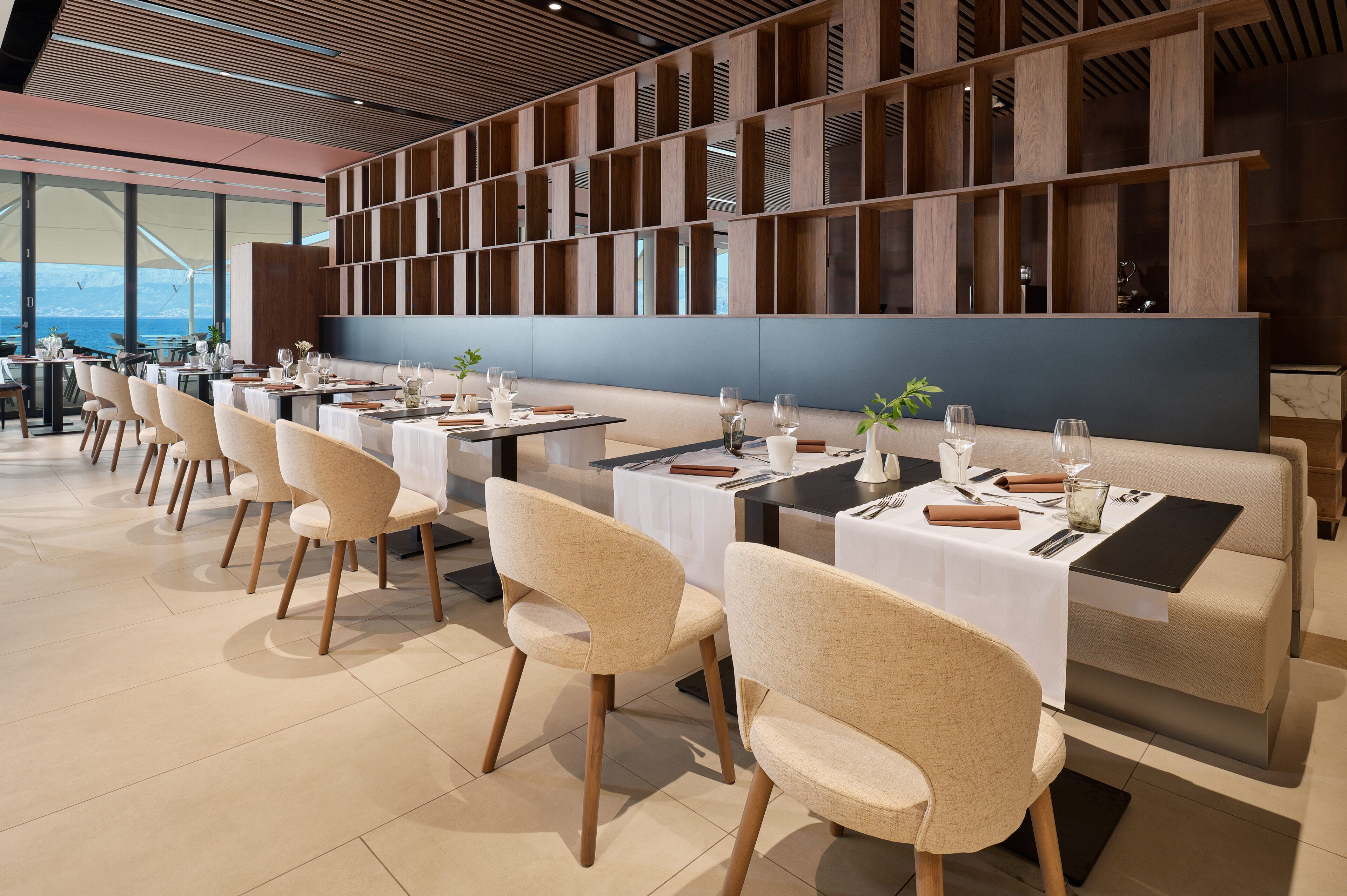En moderne restaurant med et langt spiseområde, vægge af træpaneler og havudsigt.