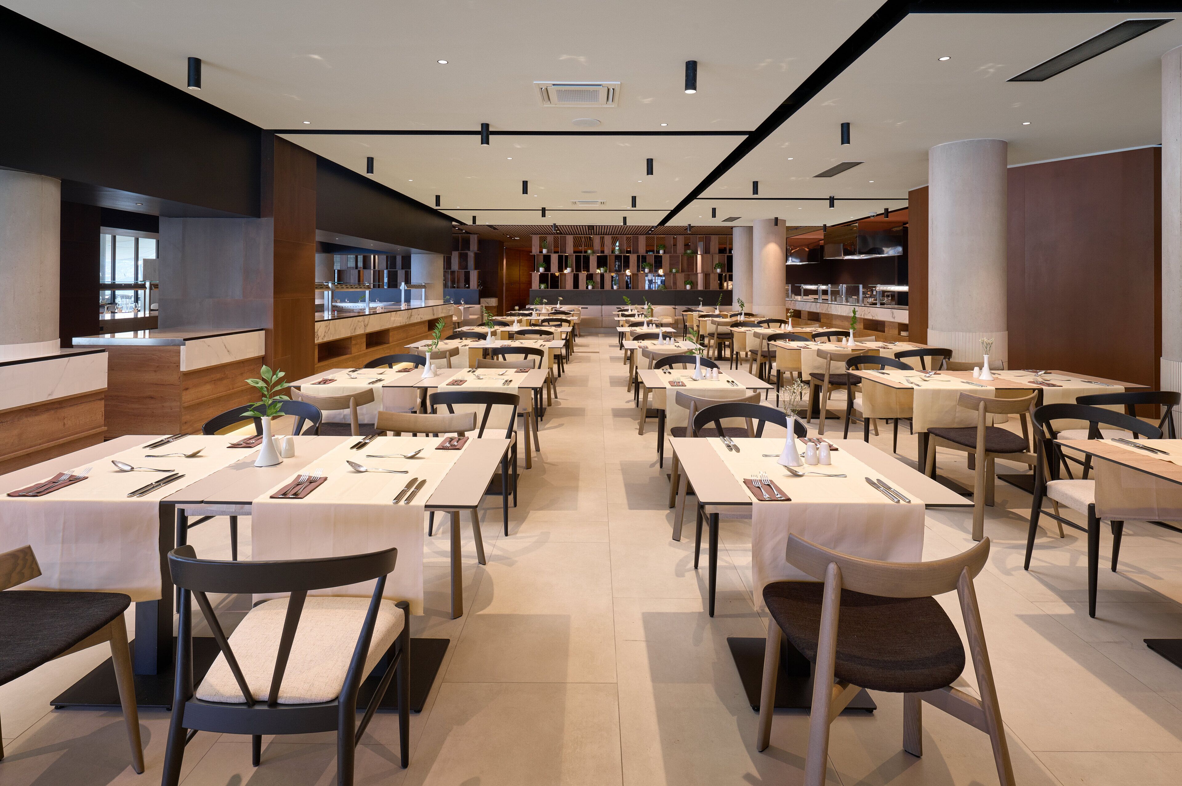 Un comedor moderno con varias mesas y sillas, una barra central, y vista a la cocina al fondo.