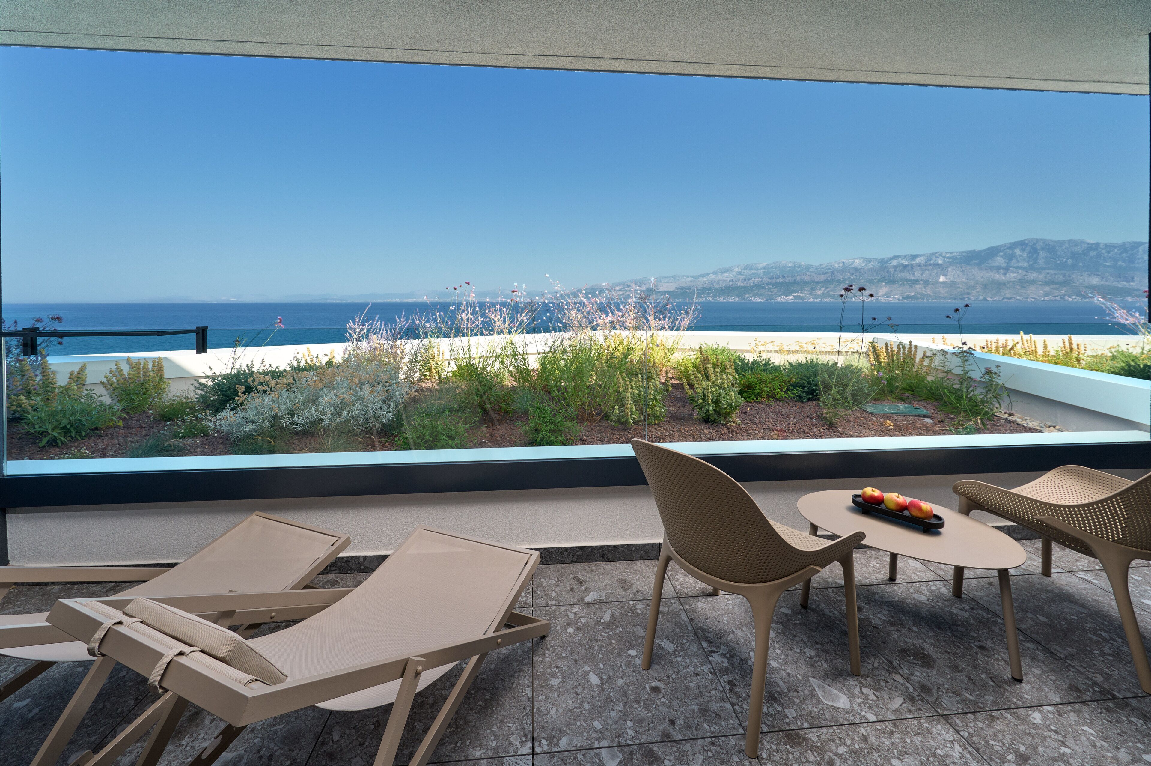 Una terraza con vistas al mar, que incluye una mesa con sillas y una pequeña mesa con fruta.