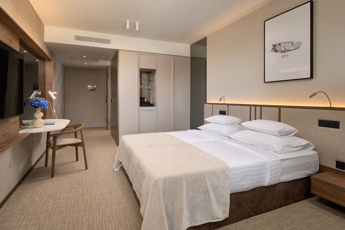 A hotel room with a bed, bedside table, desk, chair, and a mirror.