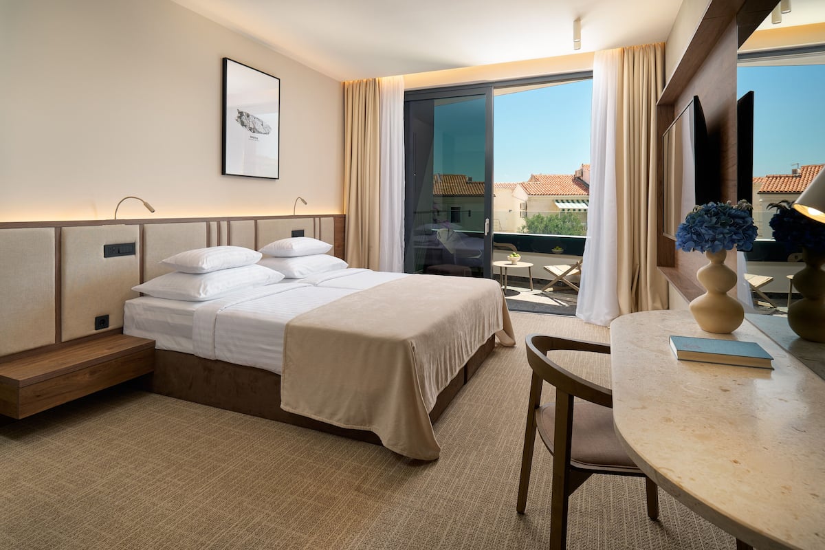 A hotel room with a bed, bedside table, and a view of the outside.