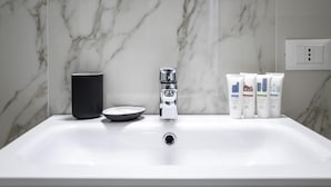 A bathroom sink with a marble backsplash, a black mug, a salt and pepper shaker, and toiletries. - Italianway - The B Village Business - 12 (Milan)