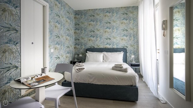 A bedroom with a bed, bedside tables, a chair, and a table with a magazine. - Italianway - The B Village Business - 12 (Milan)