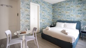 A hotel room with a bed, a small table with chairs, and a wall with a floral pattern. - Italianway - The B Village Business - 12 (Milan)