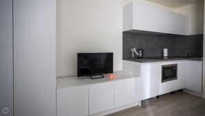 A modern kitchen with white cabinetry, a built-in microwave, and a flat-screen TV on a white countertop. - Italianway - The B Village Business - 12 (Milan)