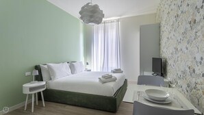 Ein modernes Hotelzimmer mit einem grünen Bett, weißen Bettwäsche, einem Flachbildfernseher und floralem Wandpapier.